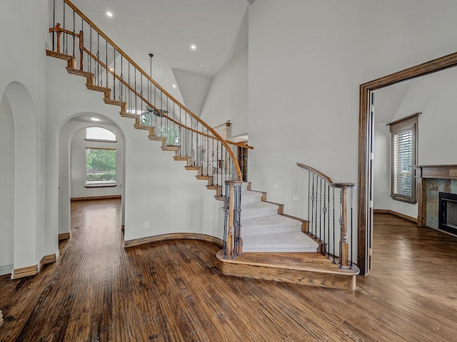 stairs featuring a tile fireplace, a high ceiling, wood finished floors, arched walkways, and baseboards
