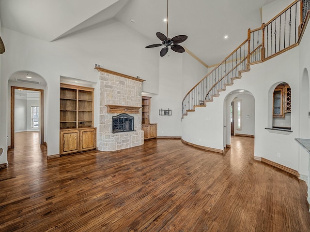 unfurnished living room featuring high vaulted ceiling, wood finished floors, ceiling fan, arched walkways, and a fireplace
