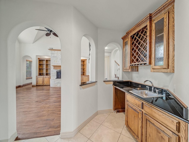 bar featuring arched walkways, baseboards, ceiling fan, and a sink