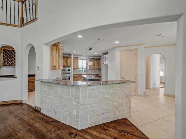kitchen featuring stainless steel appliances, arched walkways, baseboards, visible vents, and light stone counters