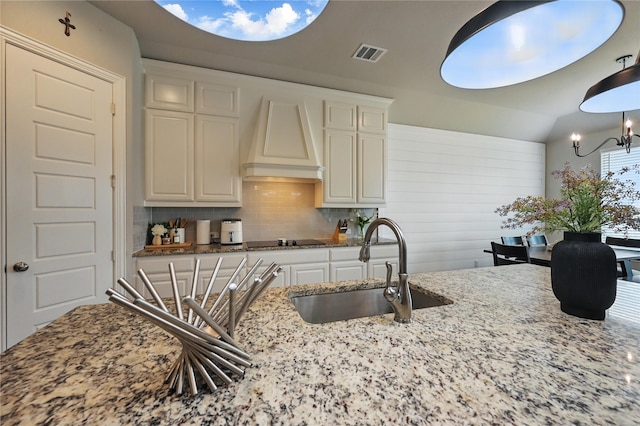 kitchen with custom range hood, tasteful backsplash, a chandelier, light stone countertops, and a sink