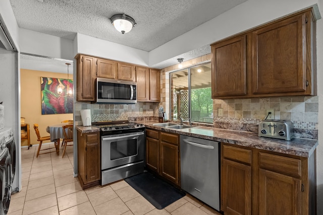 kitchen featuring stainless steel appliances, a sink, light tile patterned flooring, dark countertops, and decorative backsplash