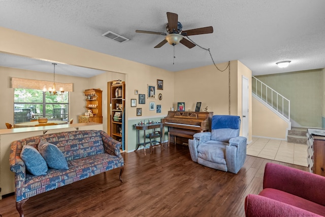 living area featuring stairway, a textured ceiling, wood finished floors, ceiling fan with notable chandelier, and visible vents