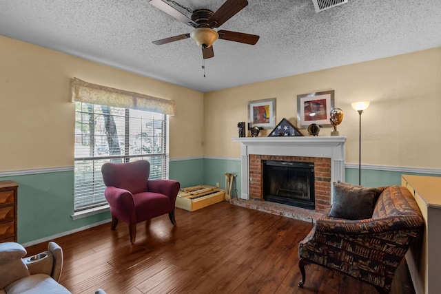 sitting room featuring visible vents, a fireplace, a textured ceiling, hardwood / wood-style flooring, and ceiling fan