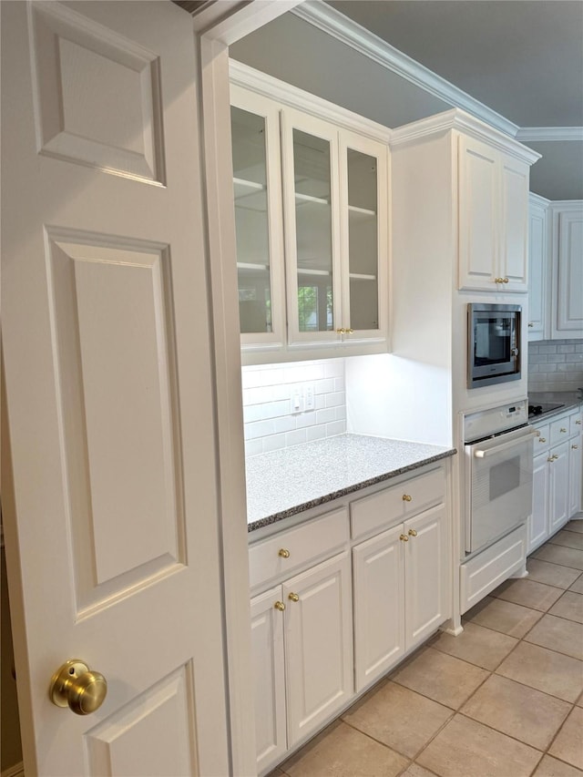 611 Twin Creek Dr, Allen, TX 75013 - kitchen featuring oven, stainless steel microwave, white cabinetry, tasteful backsplash, and ornamental molding