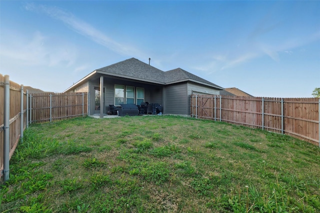 back of house featuring a garage, a yard, roof with shingles, and a fenced backyard