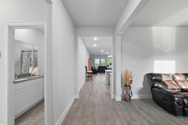 hall featuring recessed lighting, light wood-style flooring, baseboards, and a sink