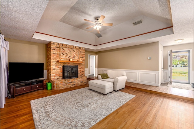 living area featuring a raised ceiling, a ceiling fan, a textured ceiling, and wood finished floors