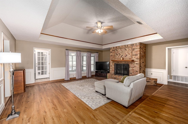 living room featuring a raised ceiling, ceiling fan, a textured ceiling, and wood finished floors