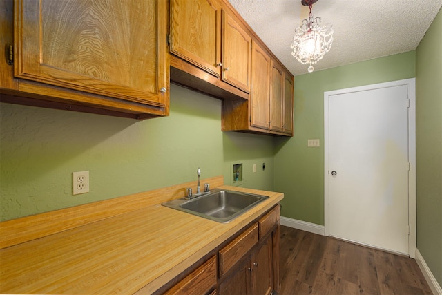 kitchen with a sink, light countertops, dark wood-style floors, baseboards, and decorative light fixtures