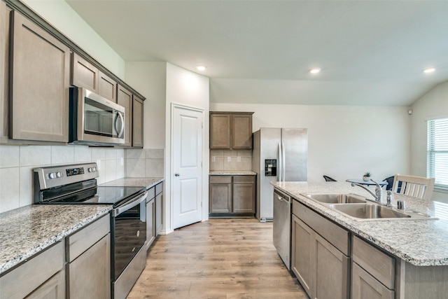 kitchen with tasteful backsplash, a sink, a kitchen island with sink, light wood-style flooring, and appliances with stainless steel finishes