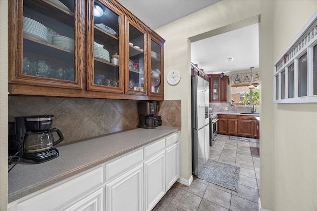 kitchen featuring a sink, light tile patterned floors, glass insert cabinets, stainless steel appliances, and backsplash