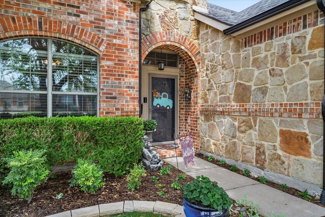 view of exterior entry featuring brick siding, stone siding, and a shingled roof