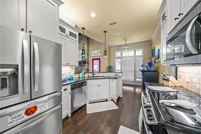 kitchen with stainless steel appliances, visible vents, ornamental molding, dark wood-type flooring, and a peninsula
