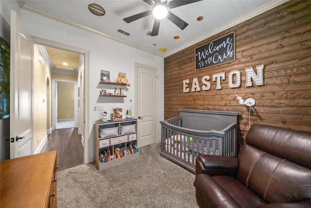 bedroom featuring carpet, wooden walls, visible vents, ornamental molding, and baseboards