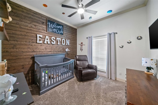 carpeted bedroom featuring baseboards, a nursery area, wood walls, ceiling fan, and ornamental molding