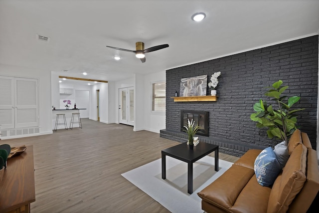 living room featuring baseboards, a ceiling fan, a brick fireplace, and visible vents