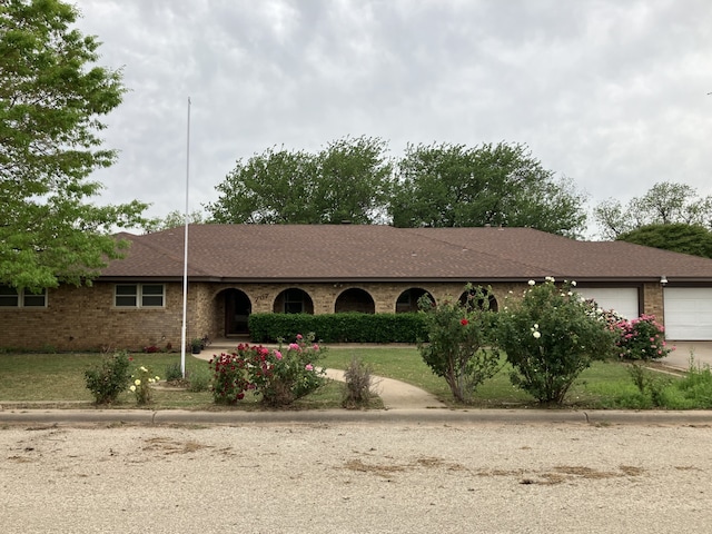 ranch-style home featuring an attached garage, brick siding, roof with shingles, and driveway