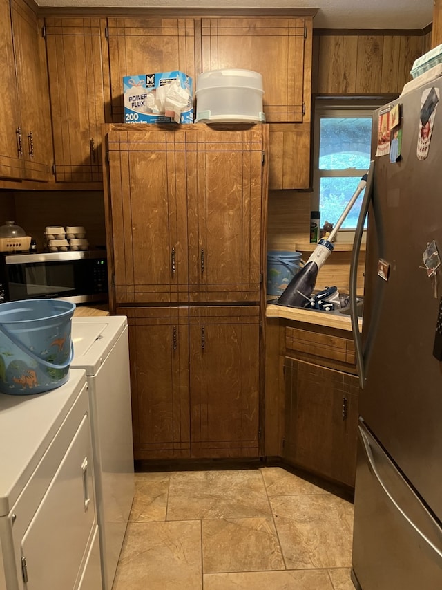 kitchen with washing machine and clothes dryer, stainless steel appliances, wood walls, brown cabinets, and light countertops