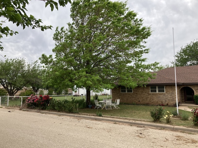 view of front of property with brick siding, fence, roof with shingles, and a front yard