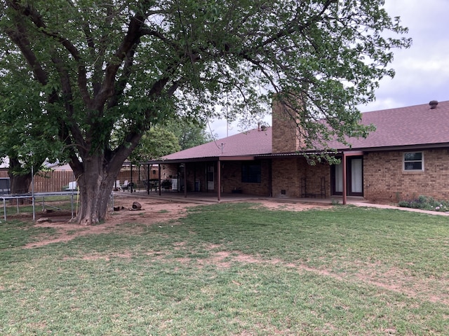 rear view of property featuring brick siding, a trampoline, a patio area, and a lawn
