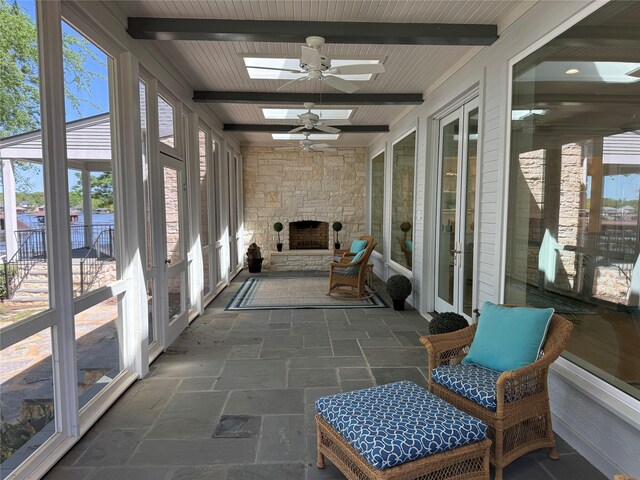 sunroom featuring ceiling fan, a skylight, beamed ceiling, and a fireplace