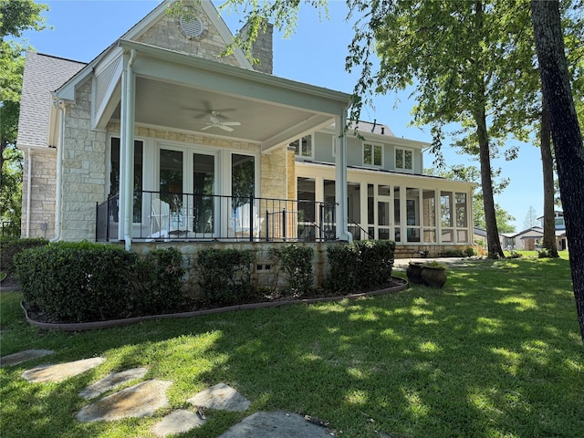 rear view of house featuring stone siding, a ceiling fan, a chimney, and a yard