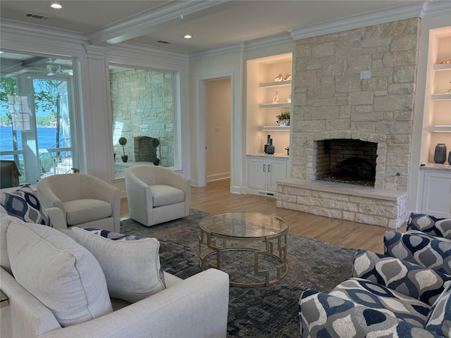 living area with wood finished floors, ornamental molding, a fireplace, built in shelves, and ceiling fan