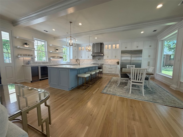 kitchen featuring white cabinets, high end appliances, wall chimney range hood, light wood-type flooring, and crown molding