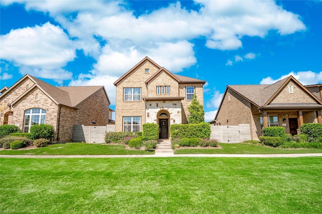 french country style house with brick siding, a front lawn, and fence