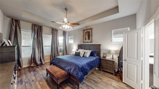 bedroom featuring light wood finished floors, baseboards, a tray ceiling, and ceiling fan