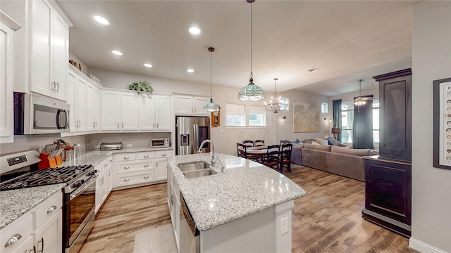 kitchen with a kitchen island with sink, light wood-style flooring, a sink, open floor plan, and appliances with stainless steel finishes