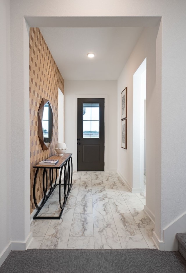 doorway to outside with marble finish floor, an accent wall, and baseboards