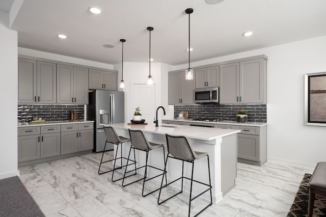 kitchen featuring a sink, gray cabinets, a breakfast bar, marble finish floor, and appliances with stainless steel finishes