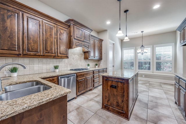 kitchen with light stone counters, a sink, hanging light fixtures, decorative backsplash, and appliances with stainless steel finishes