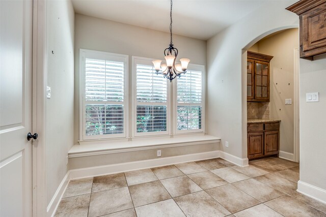 unfurnished dining area with arched walkways, a notable chandelier, baseboards, and light tile patterned flooring