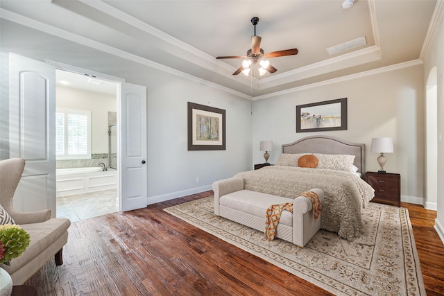 bedroom with crown molding, a tray ceiling, dark wood-type flooring, and ensuite bathroom