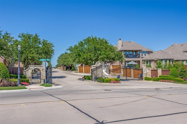 view of street with a gate, sidewalks, a gated entry, curbs, and street lights
