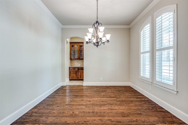 unfurnished dining area with a wealth of natural light, crown molding, wood finished floors, and a chandelier