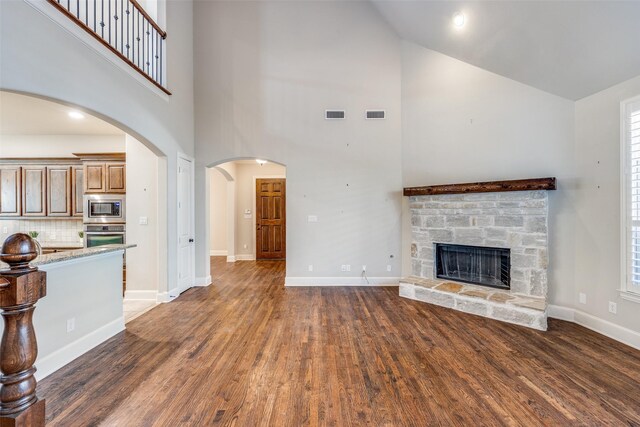 unfurnished living room featuring high vaulted ceiling, a stone fireplace, dark wood-type flooring, and visible vents