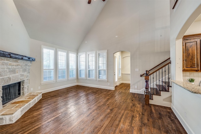 unfurnished living room featuring stairway, a stone fireplace, wood finished floors, arched walkways, and high vaulted ceiling