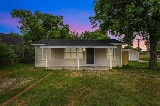 view of front facade with a detached garage, a lawn, covered porch, and roof with shingles