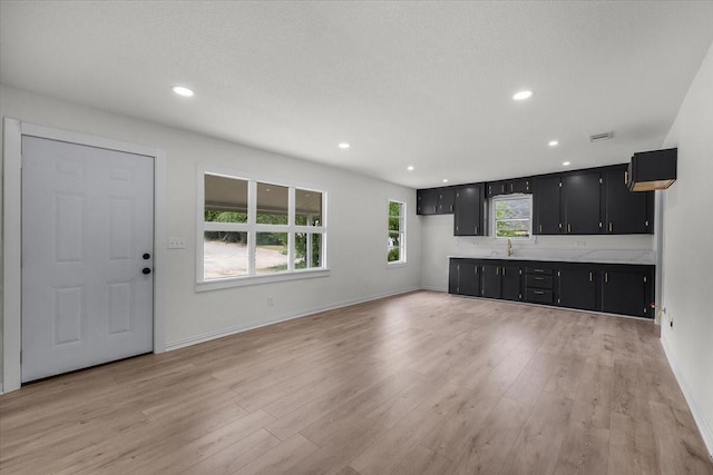 kitchen featuring recessed lighting, dark cabinets, light countertops, light wood-style floors, and baseboards