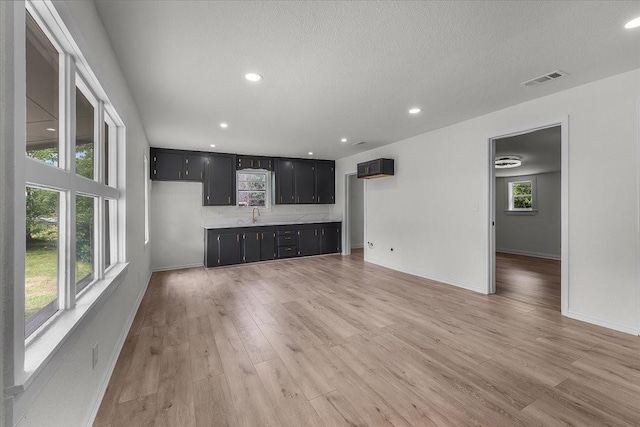 unfurnished living room featuring a sink, light wood finished floors, baseboards, visible vents, and recessed lighting
