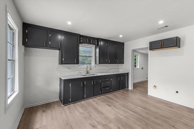 kitchen with baseboards, dark cabinets, a sink, and light countertops