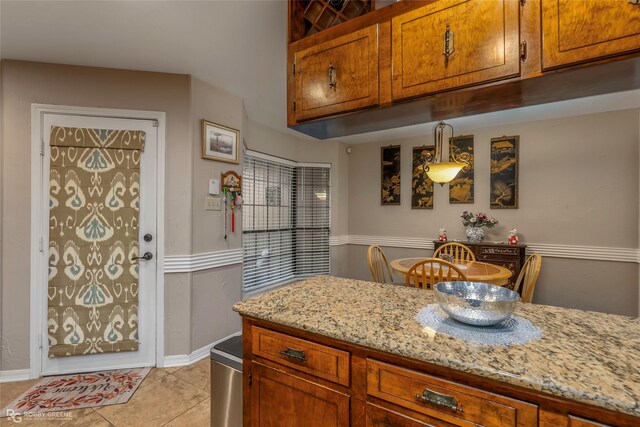 kitchen with brown cabinetry, baseboards, light stone counters, and light tile patterned floors