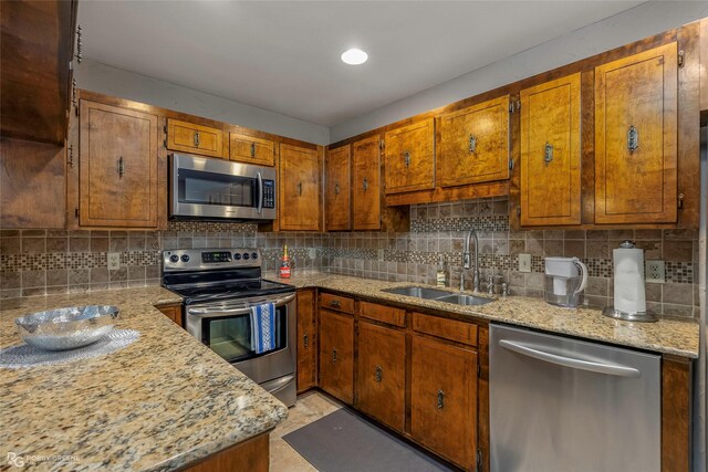 kitchen with brown cabinetry, a sink, backsplash, and appliances with stainless steel finishes