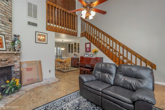 tiled living area featuring a brick fireplace, a towering ceiling, ceiling fan, and visible vents