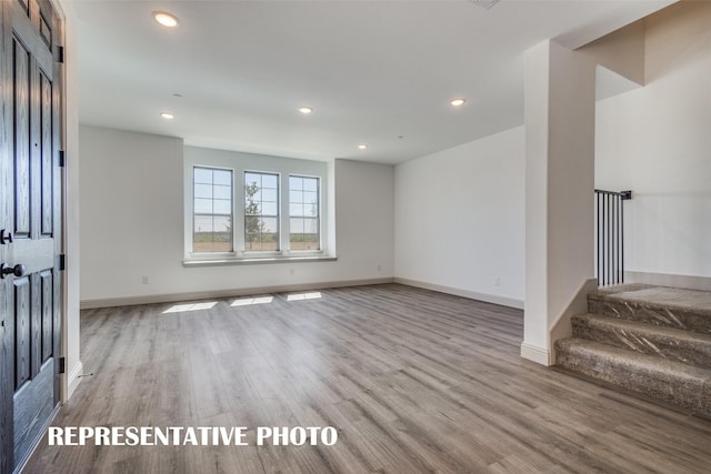 unfurnished living room with recessed lighting, baseboards, stairs, and wood finished floors