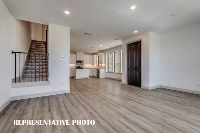 unfurnished living room with visible vents, recessed lighting, light wood finished floors, and stairway